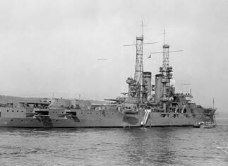 USS Utah: van slagschip tot oorlogsgraf chteraanzicht van USS Utah (BB-31) in 1912, met geschuttorens, masten en de Amerikaanse marinevlag aan de achtersteven op zee.
